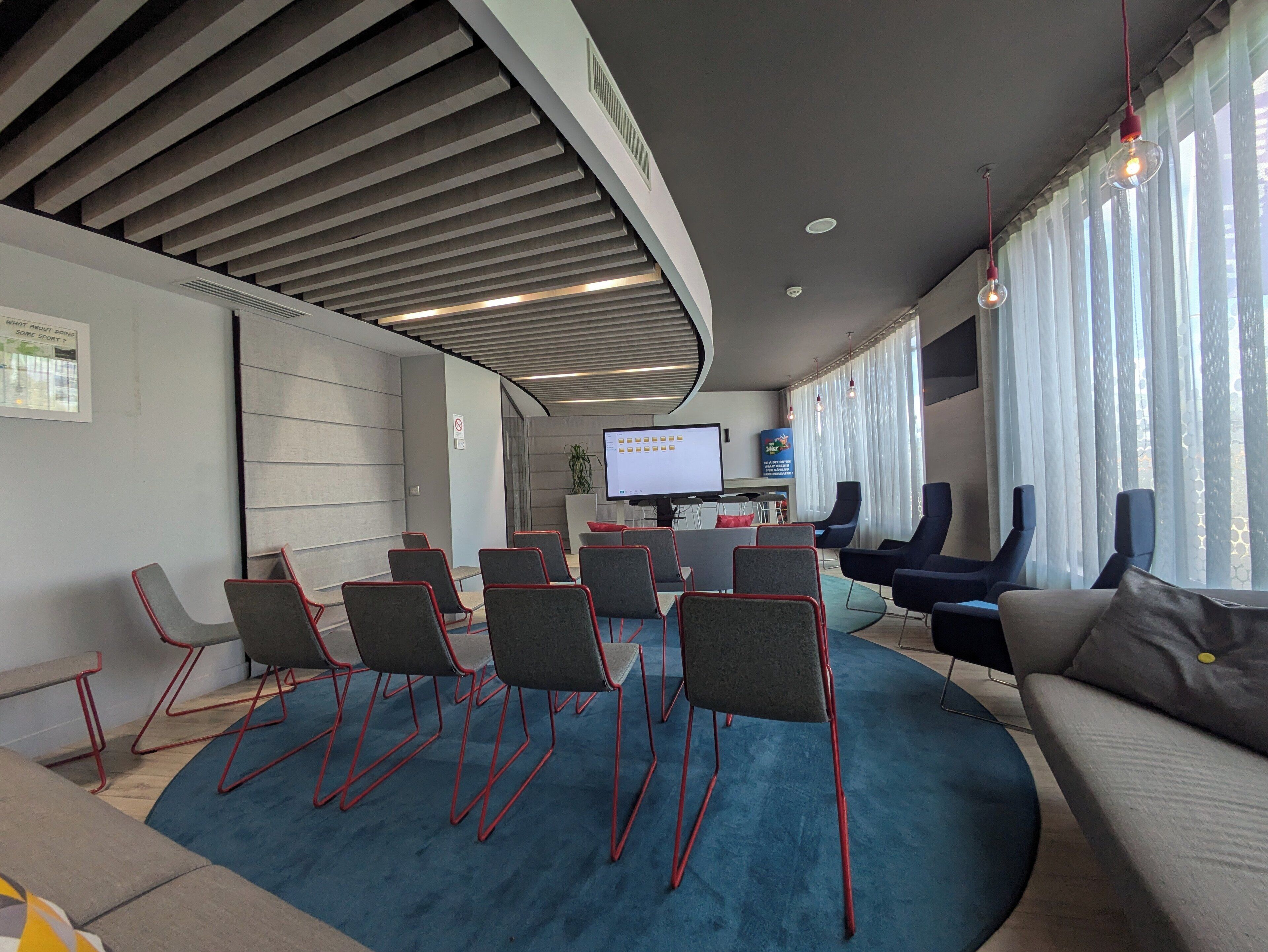 A modern conference room with a large screen, comfortable seating, and a view of the outdoors.