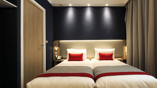 Un lit double avec deux oreillers rouges, une table de chevet avec une lampe et une porte en bois.