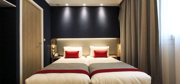 A double bed with two red pillows, a bedside table with a lamp, and a wooden door. - Holiday Inn Express Paris - Velizy by IHG (Velizy-Villacoublay)