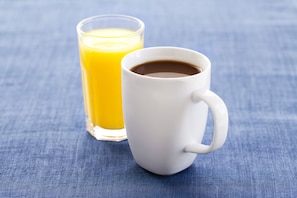 En vit mugg och ett glas apelsinjuice på en blå tygyta.