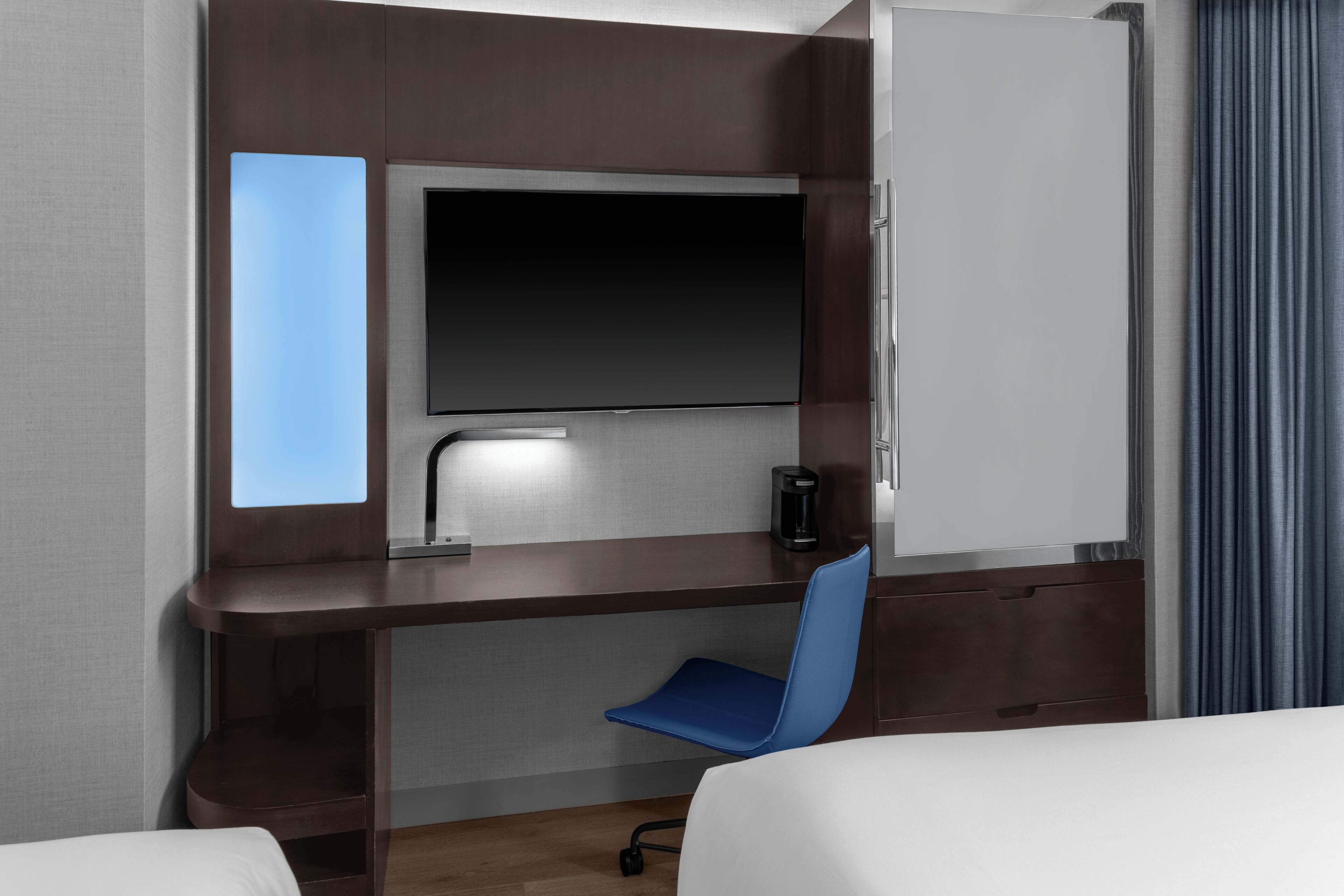 A hotel room with a bed, a desk with a chair, a flat-screen TV, a coffee maker, and a wardrobe.