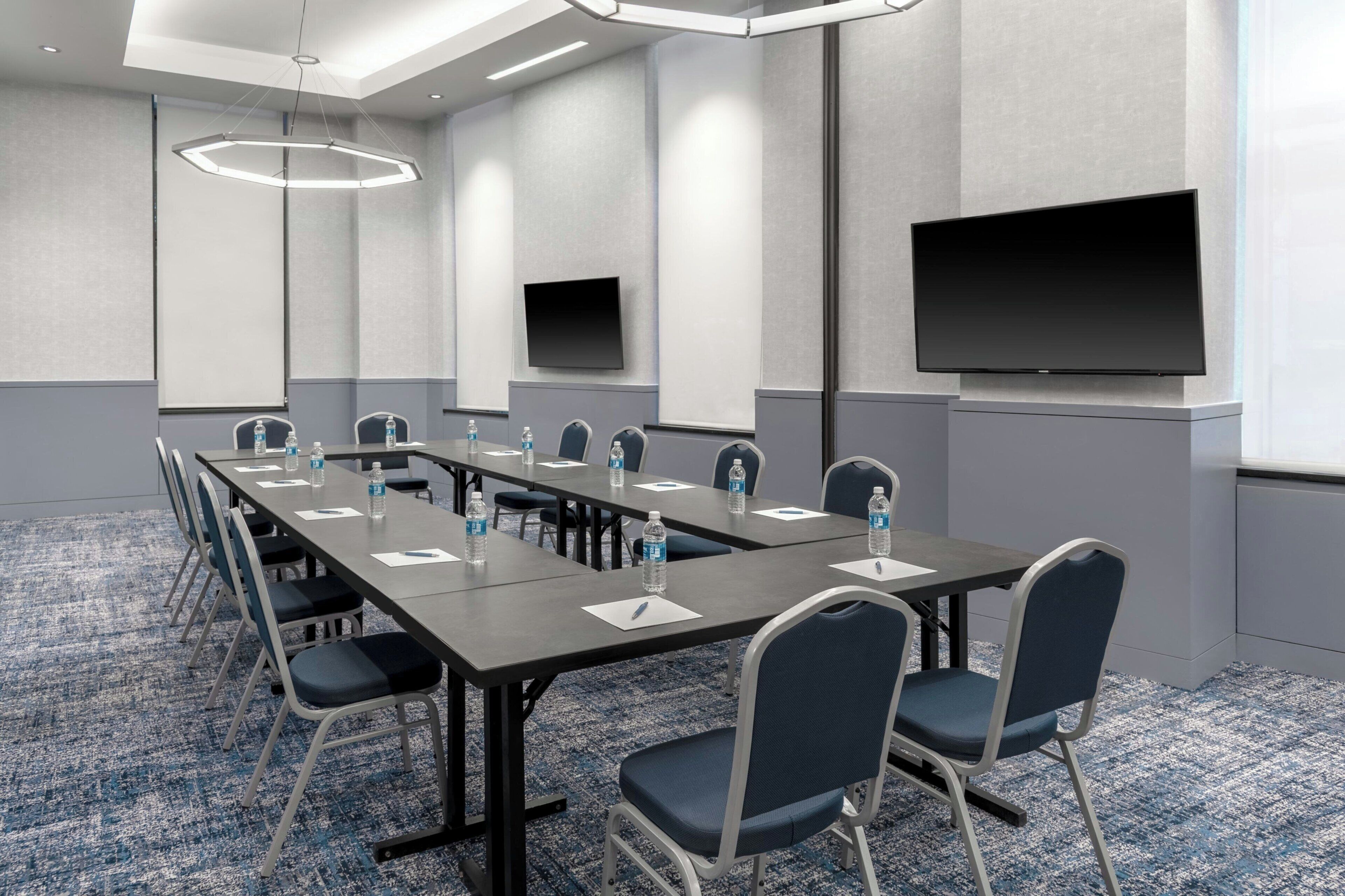 A conference room with a long table, chairs, water bottles, a projector screen, and a flat-screen TV.