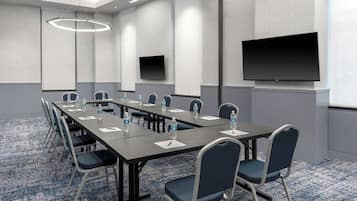 A conference room with a long table, chairs, water bottles, a projector screen, and a flat-screen TV.