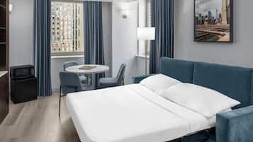 A hotel room with a bed, a desk, a chair, a lamp, and a cityscape painting.