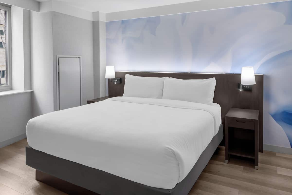 Ein modernes Hotelzimmer mit einem großen Bett, zwei Nachttischen mit Lampen, einer Tür und einer Wand mit einem blauen, abstrakten Muster.