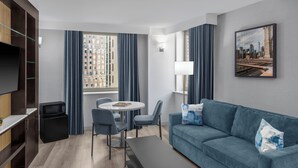 Une chambre d’hôtel moderne équipée d’un canapé, d’une table à manger, de chaises, d’un téléviseur, d’un four à micro-ondes et d’une fenêtre avec des rideaux.