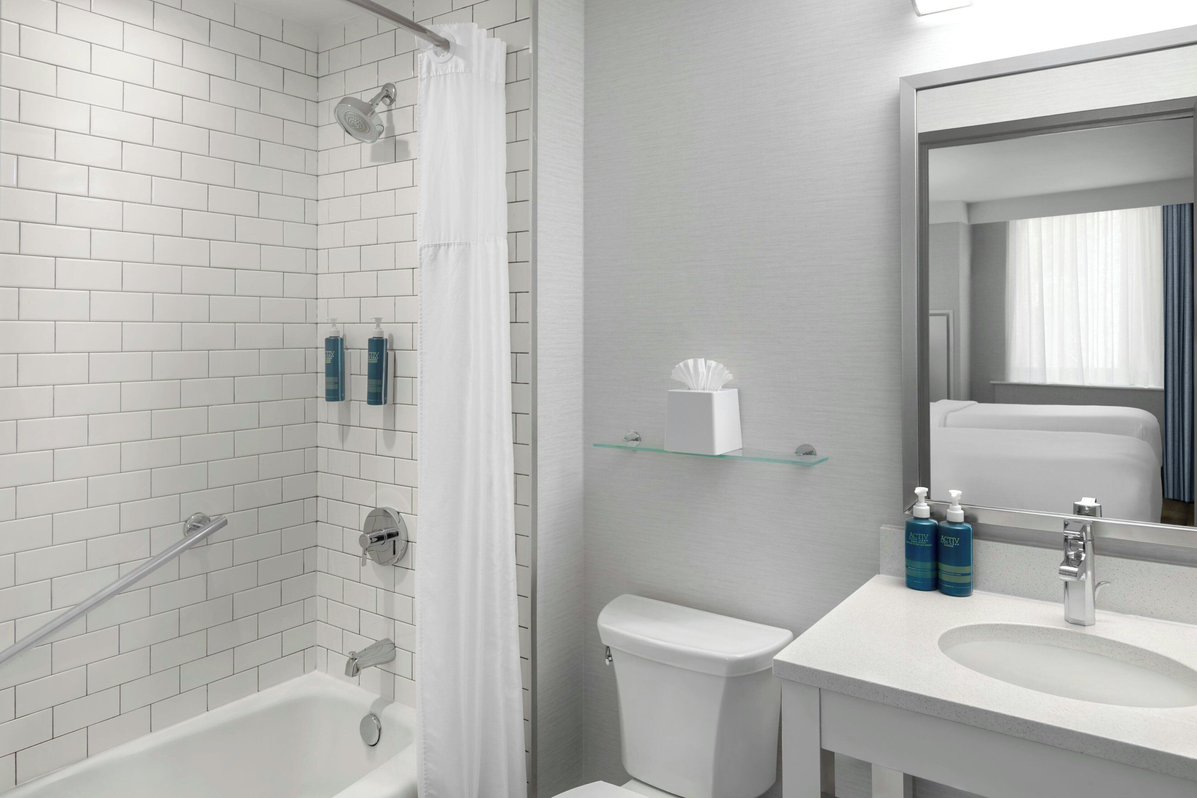 A modern bathroom with white subway tiles, a glass shower enclosure, a white toilet, and a sink with a mirror above it.