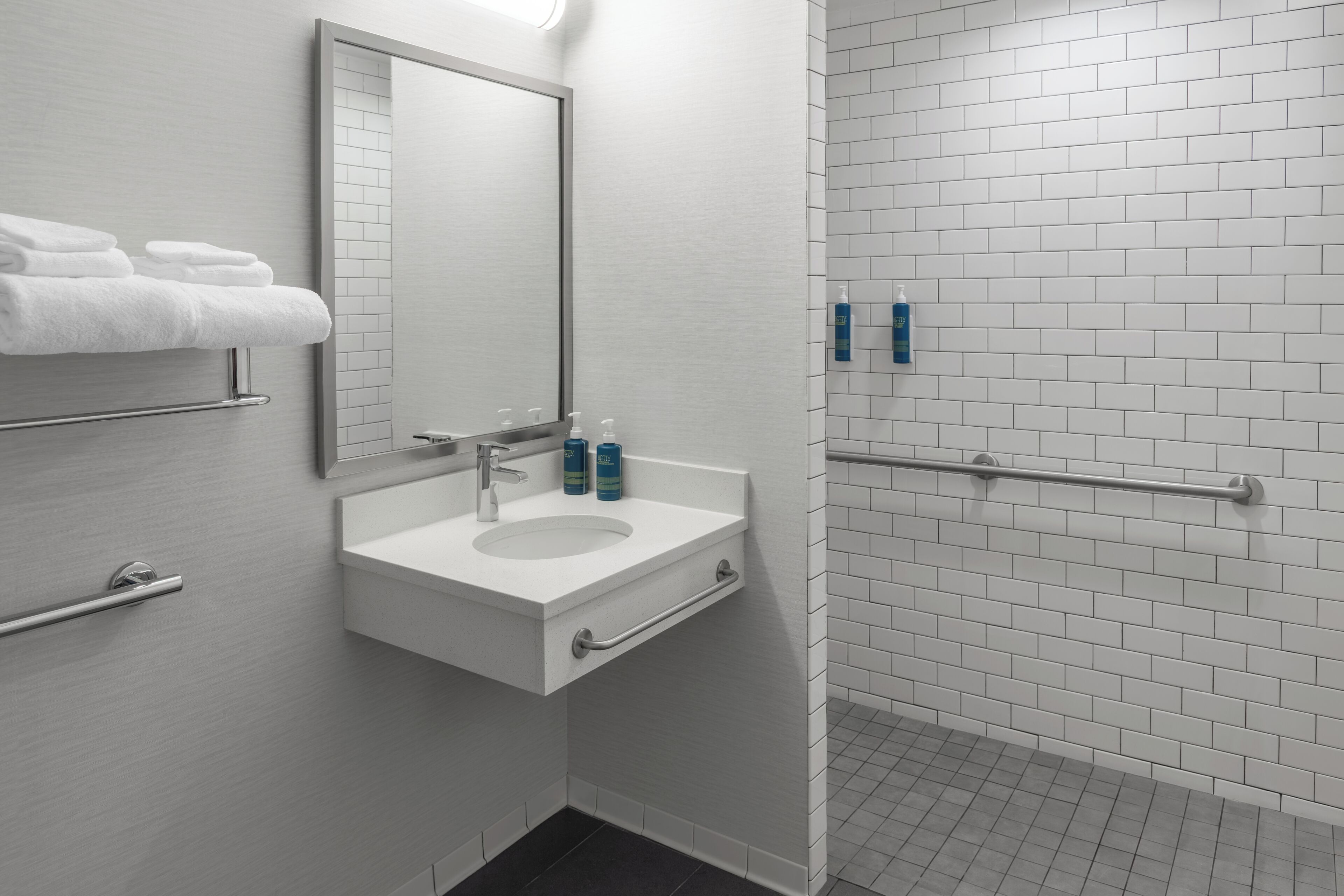 Une salle de bain équipée d’un lavabo, d’un miroir, d’un porte-serviettes et de distributeurs de gel hydroalcoolique.
