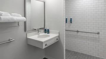 Une salle de bain équipée d’un lavabo, d’un miroir, d’un porte-serviettes et de distributeurs de gel hydroalcoolique.