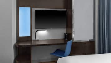 Quarto de hotel com cama, escrivaninha com cadeira, televisão de tela plana, cafeteira e janela com cortinas.