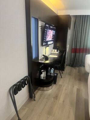 Habitación de hotel con escritorio, televisión de pantalla plana montada en la pared, lavamanos pequeño y una silla.
