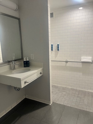A modern bathroom with a white sink, mirror, and tiled shower wall. - Four Points By Sheraton New York Downtown (New York)