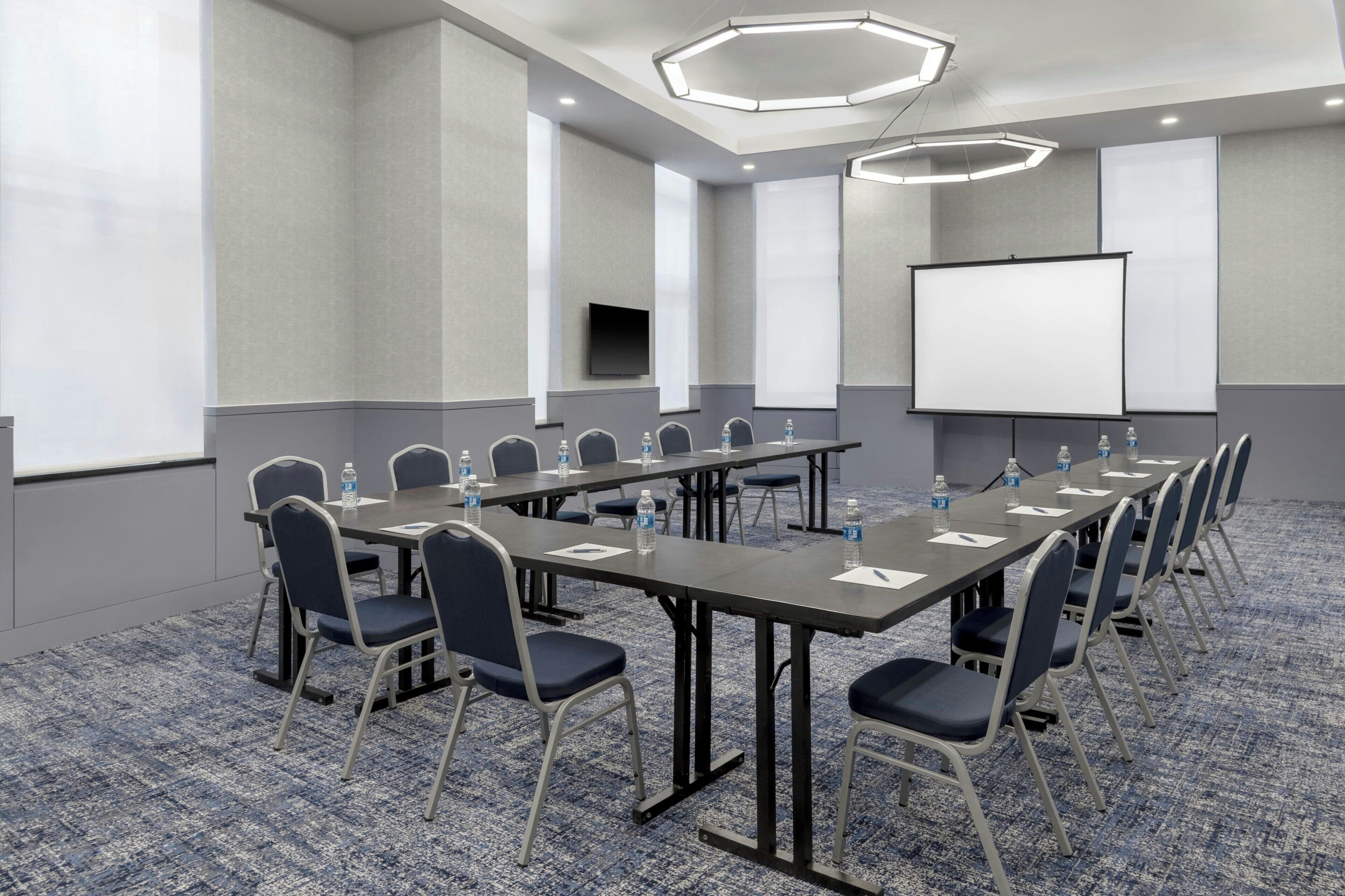 Una sala de conferencias con una larga mesa, sillas, una pantalla de proyector y una televisión.