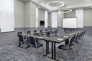 A conference room with a long table, chairs, a projector screen, and a television.