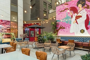 An outdoor seating area with wicker chairs and tables, a red umbrella, and a mural of a woman holding a fan.