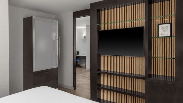 Une chambre d’hôtel moderne équipée d’une armoire, d’un téléviseur et d’un tableau encadré au mur.