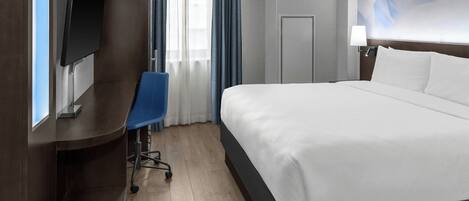 A hotel room with a bed, a desk, a chair, a television, a door, and a window with curtains.