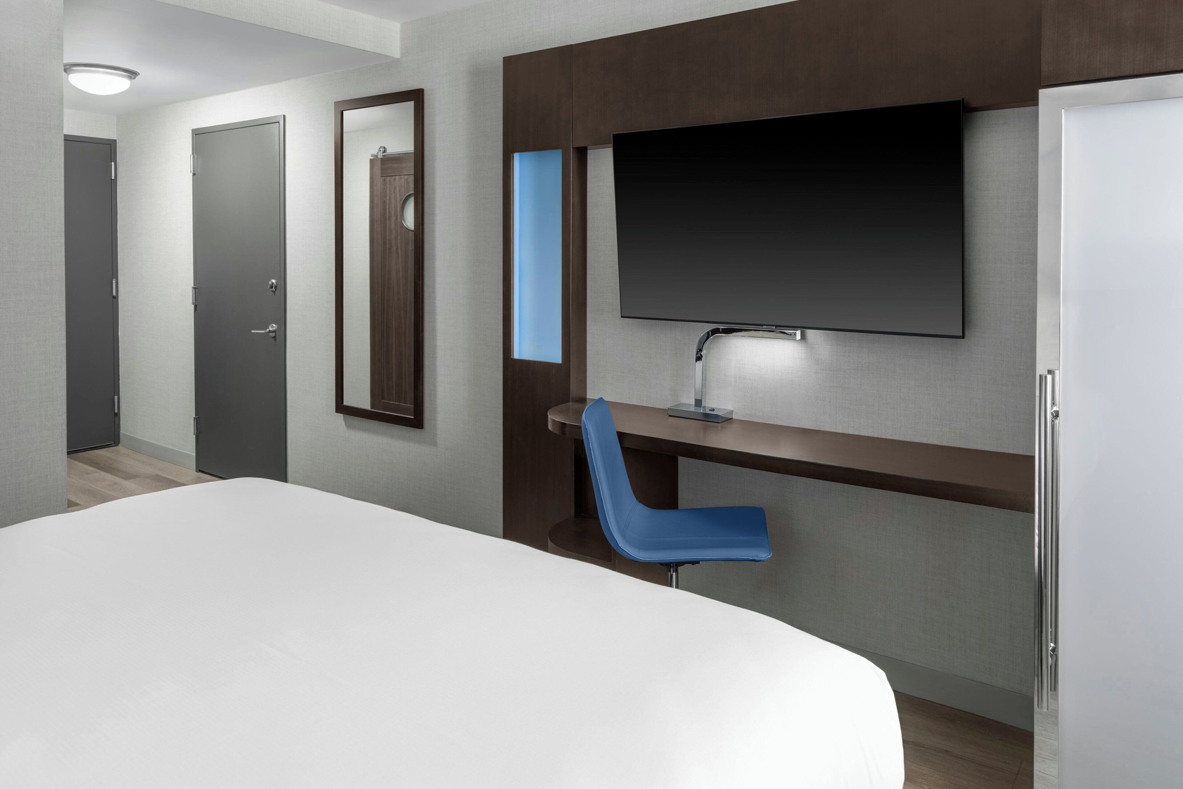 A hotel room with a bed, a desk with a chair, a TV, and a door.