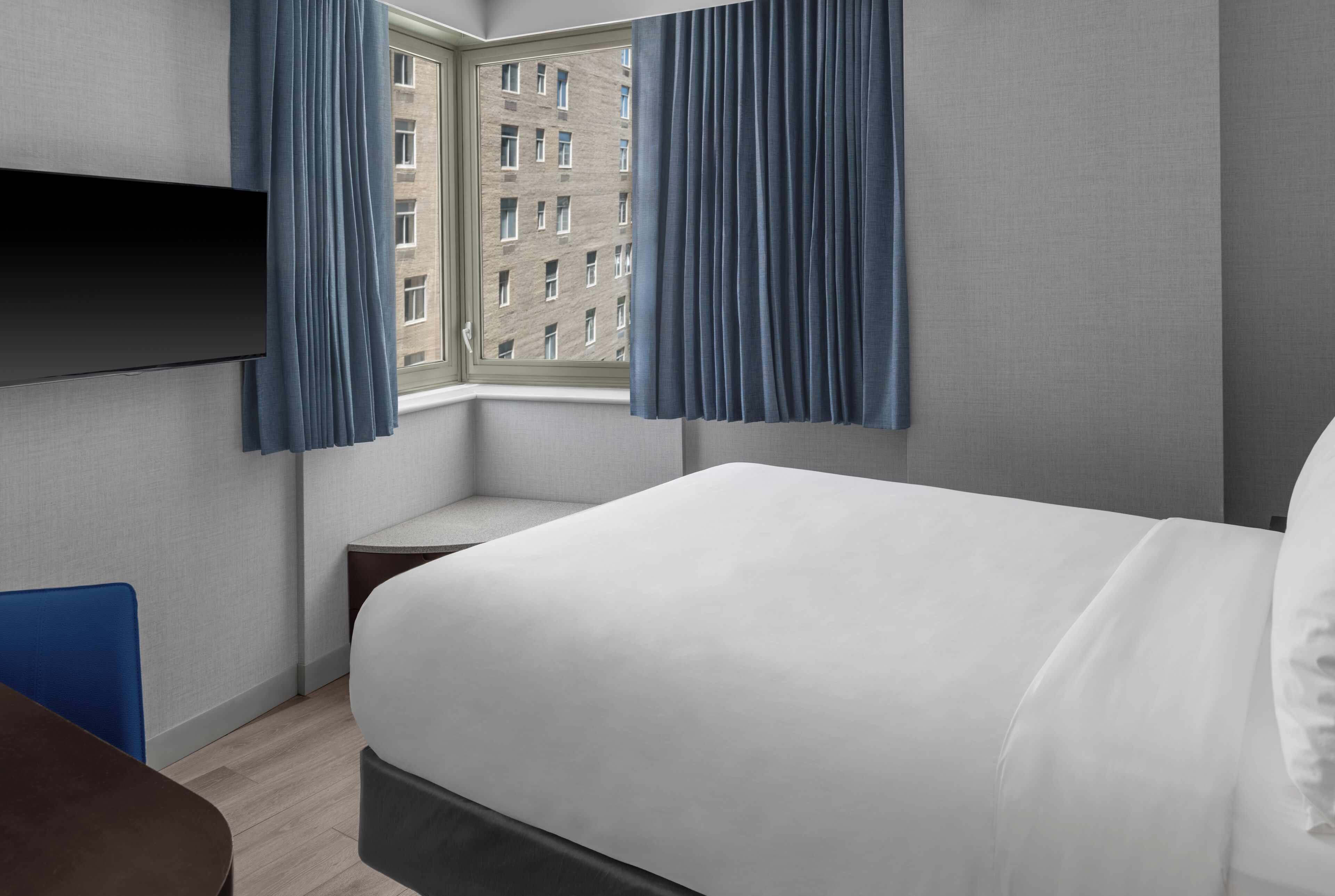 Ein Hotelzimmer mit Bett, Schreibtisch, Stuhl, Flachbildfernseher und einem Fenster mit Vorhängen.