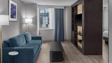 A modern living room with a blue sofa, a small round table, a dark coffee table, a floor lamp, a window with curtains, and a built-in bookshelf.