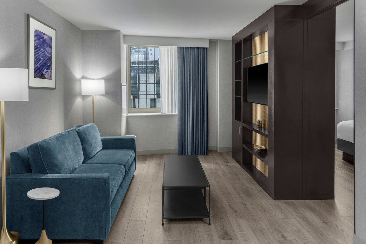 Un salon moderne avec un canapé bleu, une lampe sur pied, une table basse, une bibliothèque et une fenêtre avec des rideaux.
