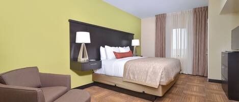 Una habitación de hotel con cama, una silla, una mesita de noche con lámparas y un escritorio.