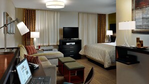 A hotel room with a bed, a desk with a laptop, a TV, a dresser, and a chair. - Staybridge Suites Tomball - Spring Area by IHG (Tomball)