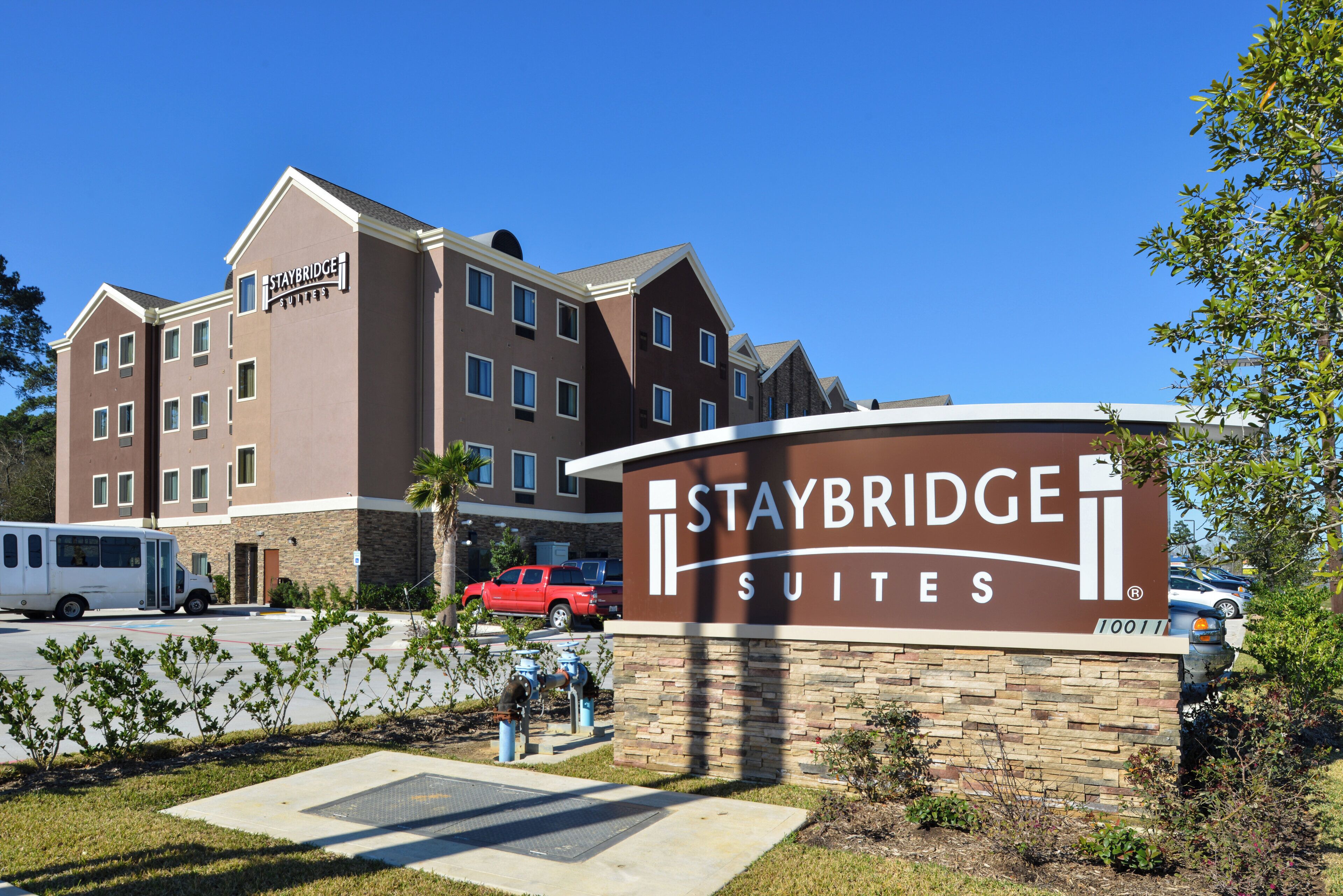 A Staybridge Suites hotel with a sign, parking area, and a red vehicle.