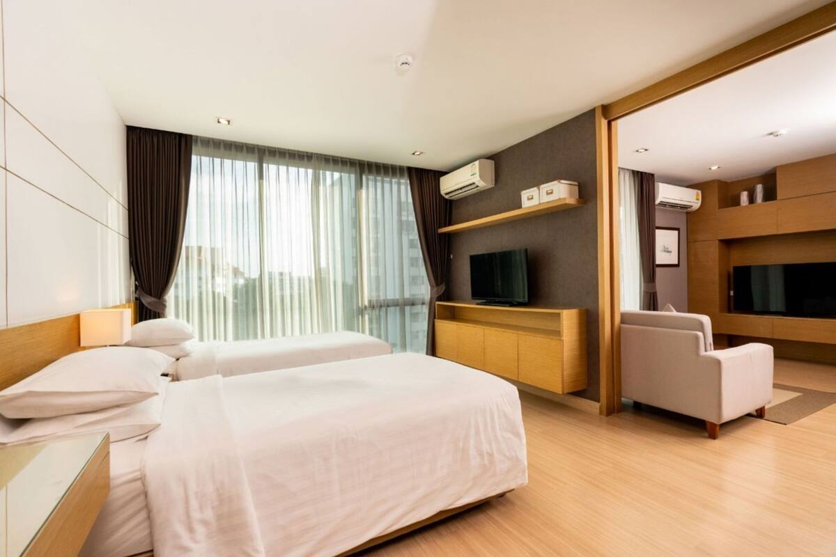 A hotel room with a bed, a desk, a TV, a chair, and an air conditioning unit.