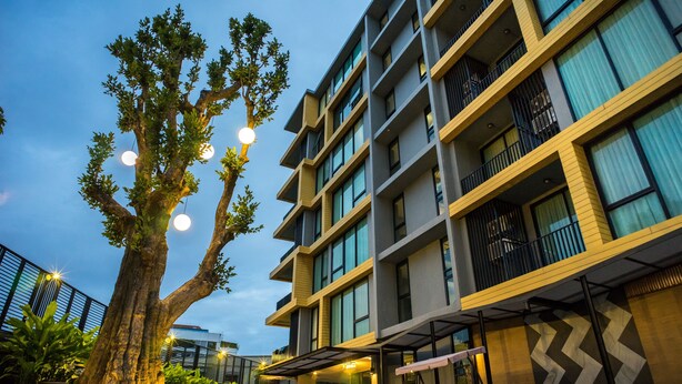 A modern building with multiple balconies, large windows, and a tree in the foreground. - Sanae' Hotel Nimman (Chiang Mai)