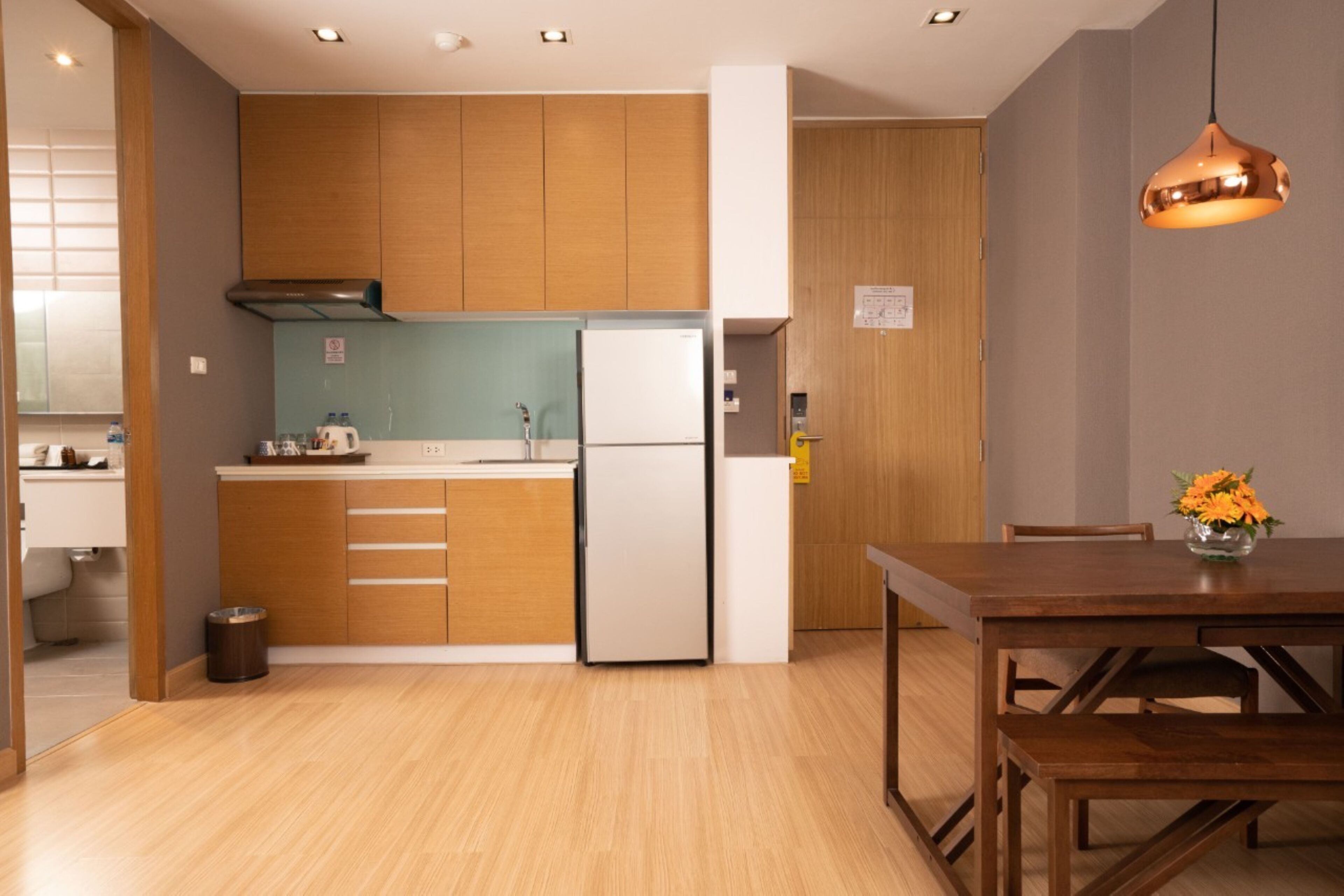 A modern kitchen with wooden cabinets, a white refrigerator, and a dining area with a wooden table and chairs.