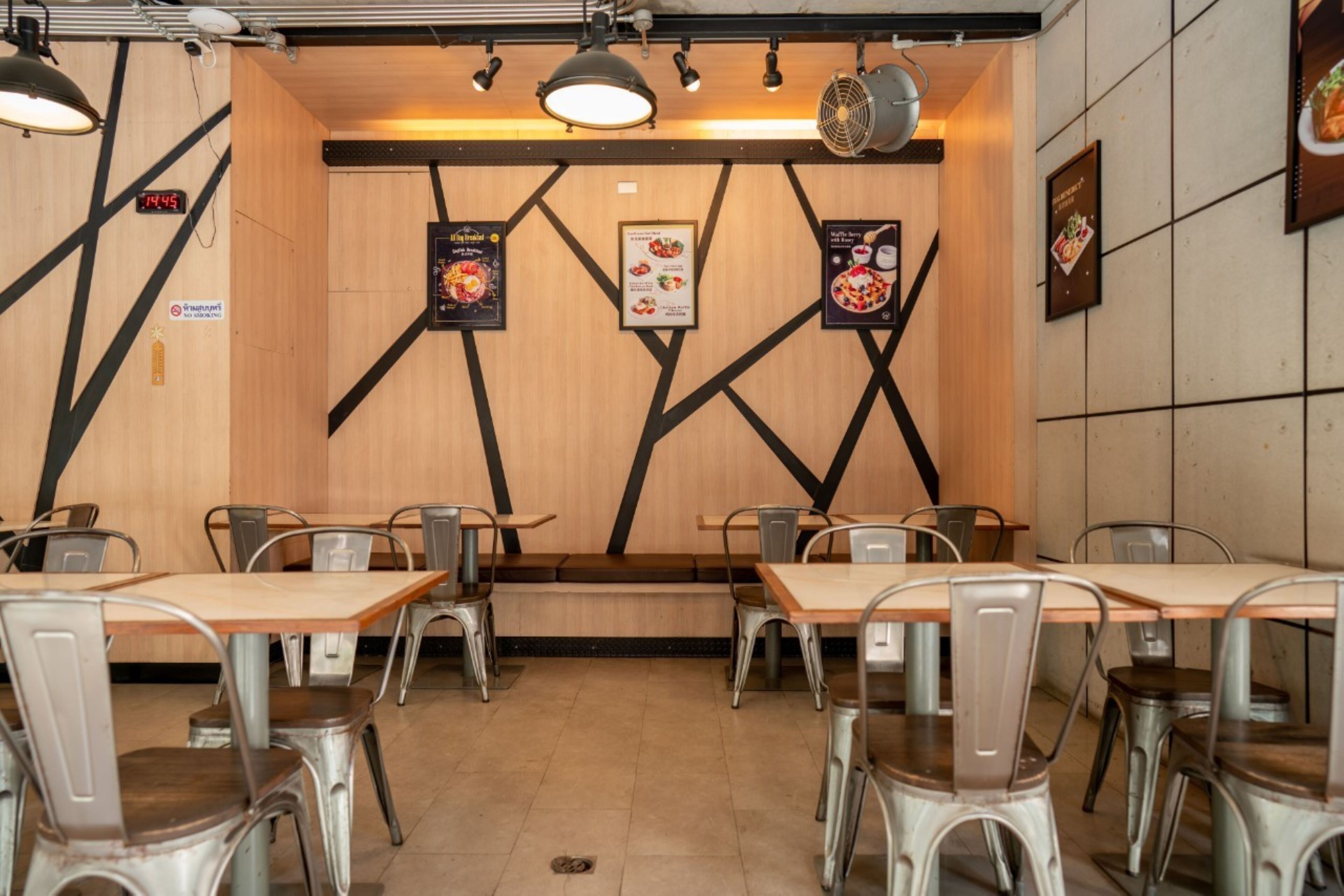 A restaurant interior with wooden walls, metal chairs, and tables. There are menu boards on the walls and a clock on the left.