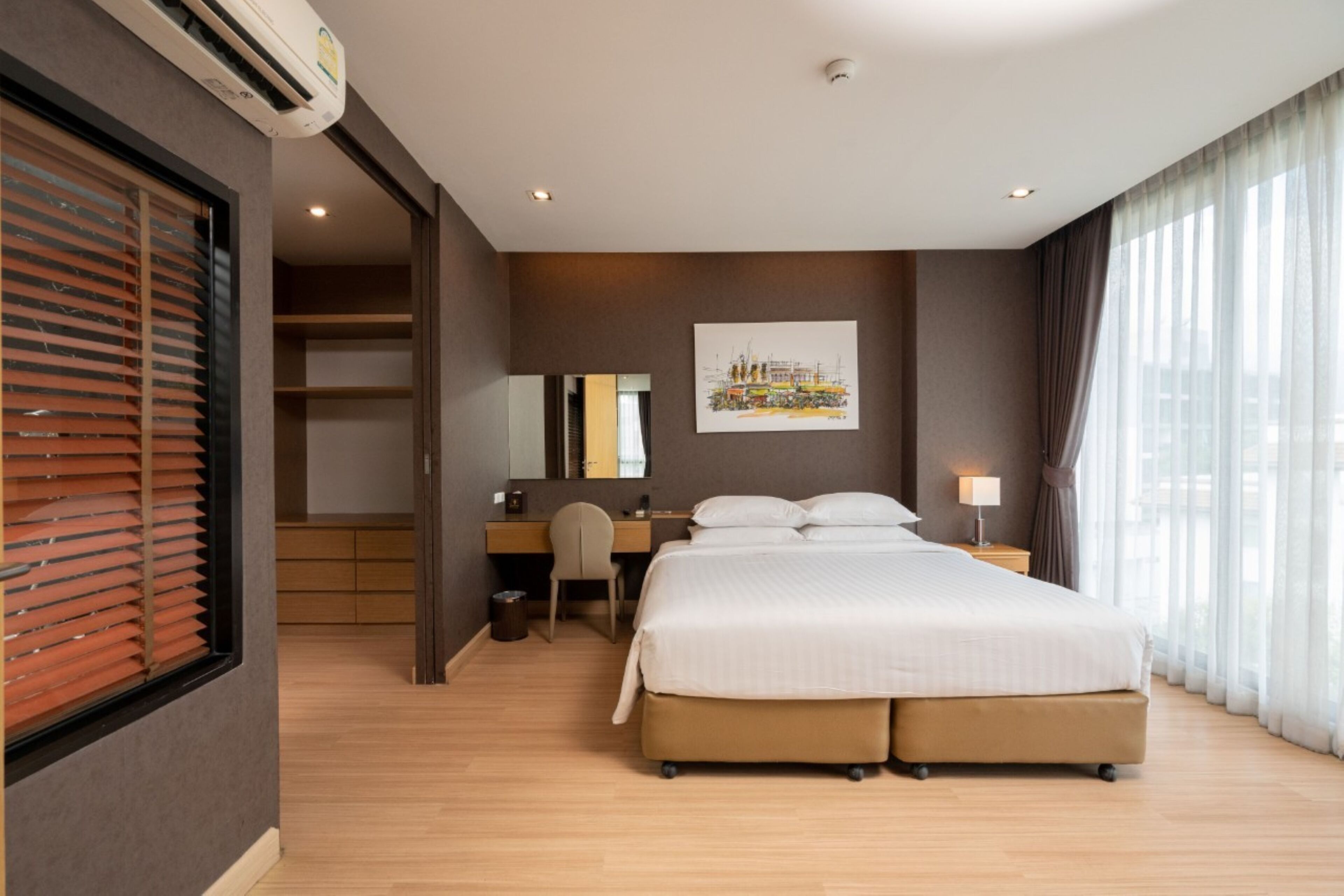 A hotel room with a bed, a desk, a chair, a mirror, and a window with curtains.