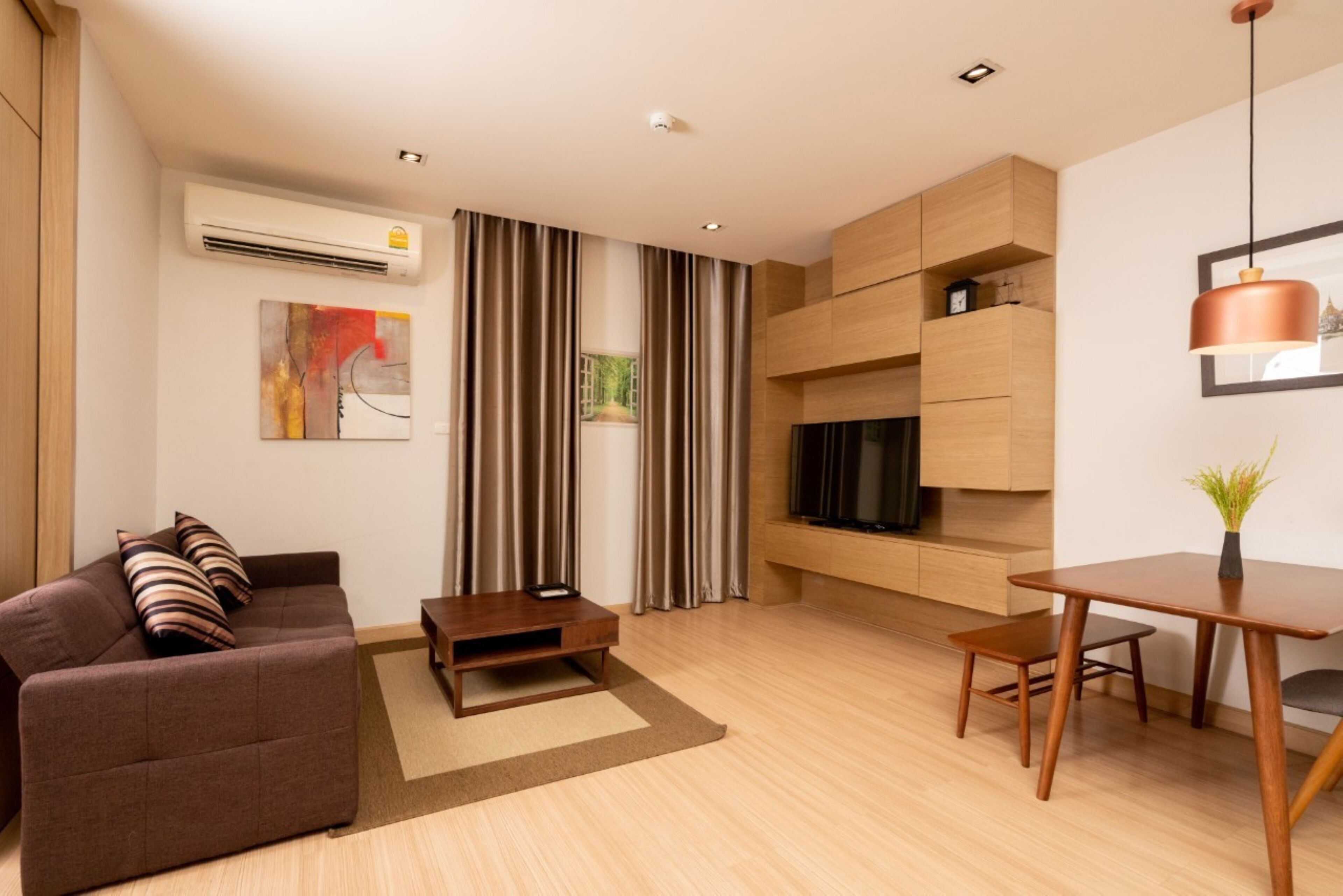 A modern living room with a sofa, a coffee table, a TV mounted on a wooden wall, and a dining area with a table and chairs.