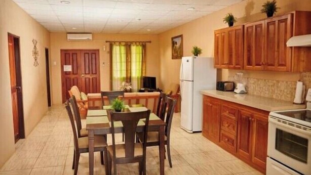 A compact kitchen with wooden cabinets, a refrigerator, and a dining area with a table and chairs. -  JB'S SERENITY STAY (Carnbee)