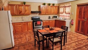 A compact kitchen with wooden cabinets, a stove, microwave, and a dining table with chairs. -  JB'S SERENITY STAY (Carnbee)