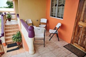 Un balcón con escalera de madera, sillas blancas y una planta en maceta.