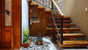 Un escalier en bois adossé à un mur en pierre, une porte en bois avec une fenêtre, et un petit espace jardin agrémenté de galets et de plantes.