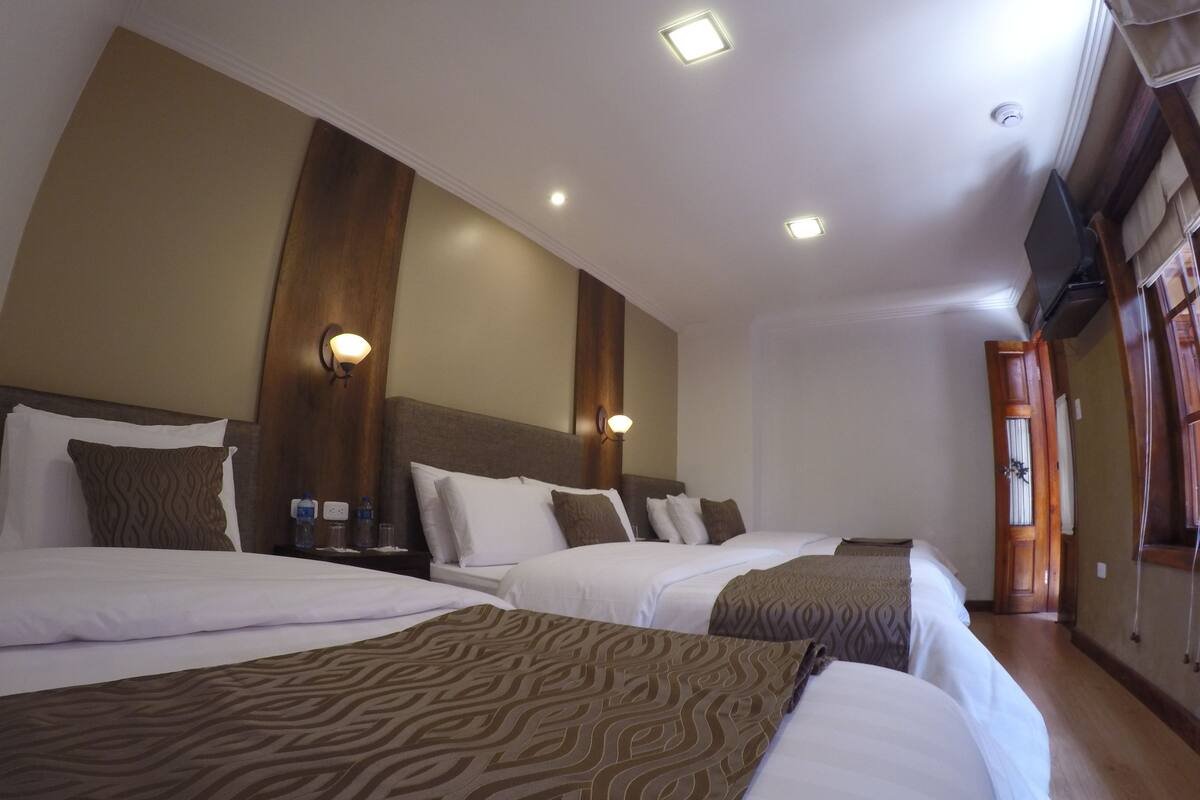 Ein Hotelzimmer mit zwei Betten, einem Holzkopfstück, einem an der Wand montierten Fernseher und einer Holztür.