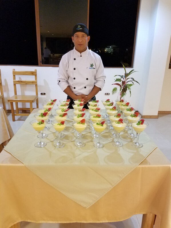 Un chef de pie detrás de una mesa con varios vasos de postres dispuestos en filas.
