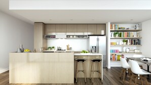 A modern kitchen with a central island, bar stools, a built-in bookshelf, and a dining area with a table and chairs. - Clayton Serviced Apartments (Clayton)