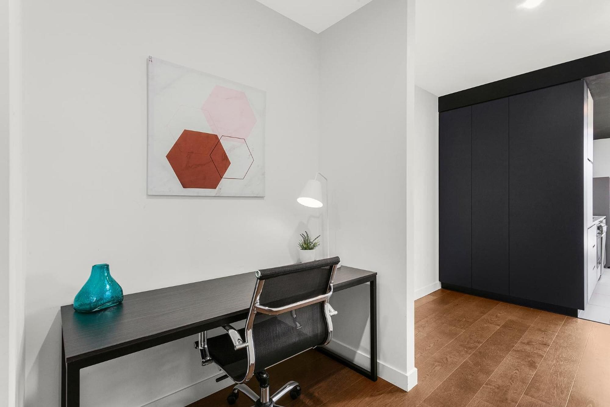A modern office space with a desk, chair, and a wall-mounted lamp.