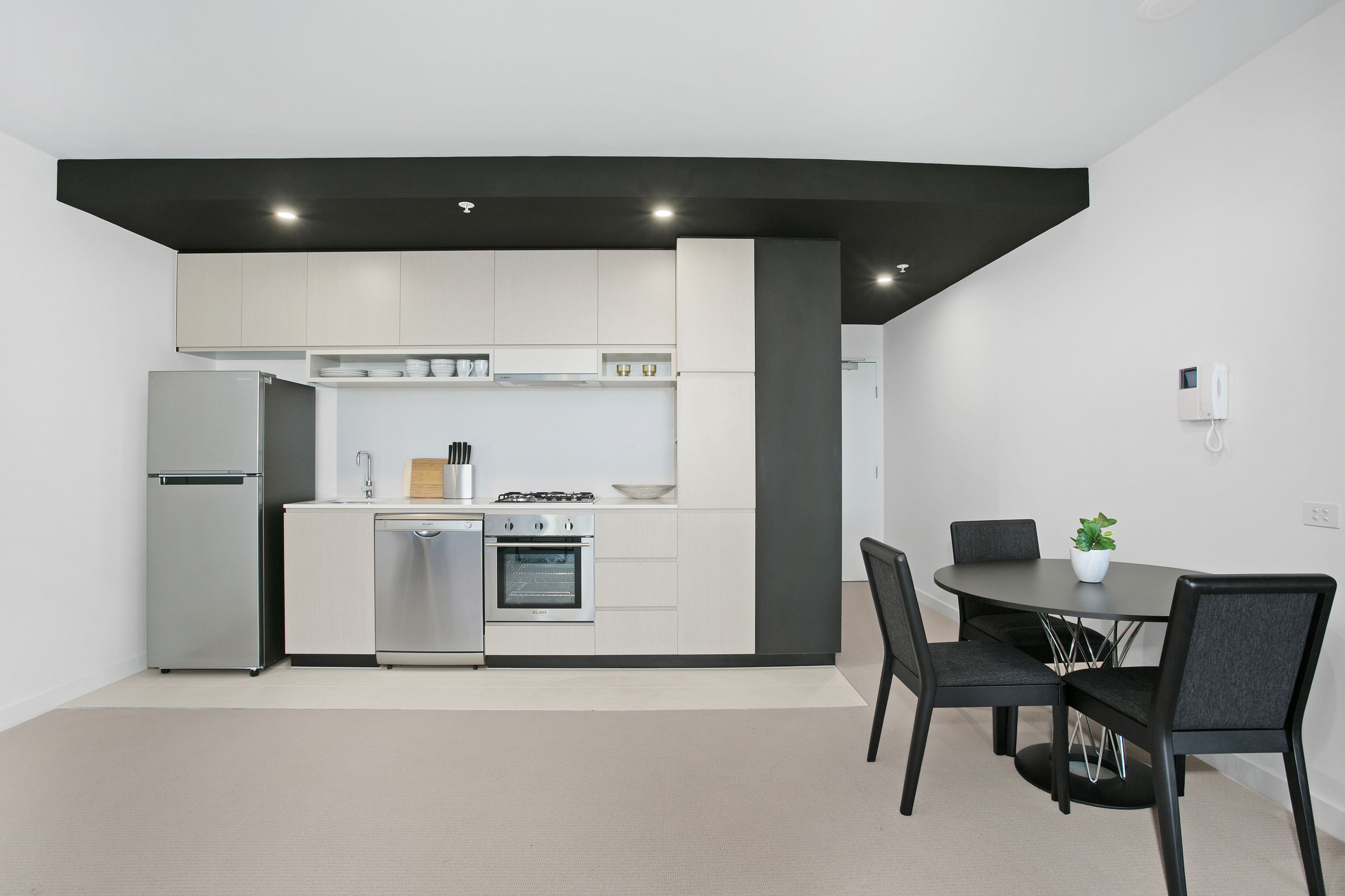Una cocina moderna con armarios blancos, horno empotrado y comedor con mesa y sillas.