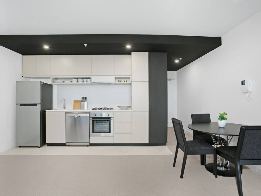 Une cuisine moderne avec des meubles blancs, un four encastré et un coin repas comprenant une table et des chaises.