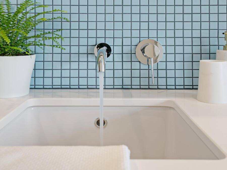A bathroom with a white sink, a potted plant, and a blue tiled backsplash.