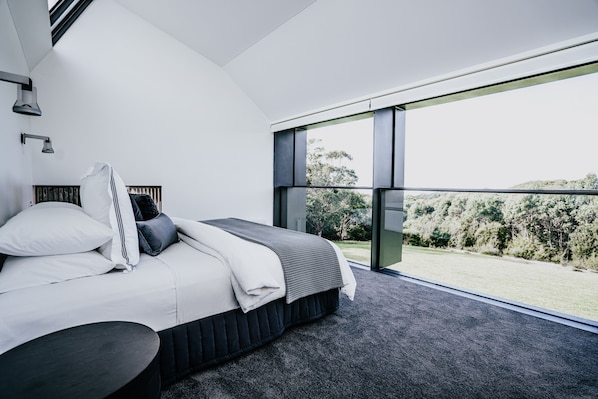 Un dormitorio moderno con una cama grande, vista a un área verde y un tragaluz.