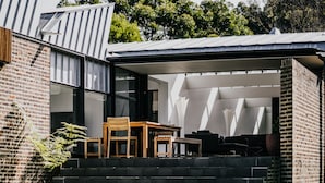 A modern building with a brick exterior, a set of outdoor stairs leading to a covered seating area with a table and chairs. - Alkina Lodge (Wattle Hill)