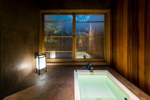 A bathroom with a large window, a bathtub, and a small table with a light.
