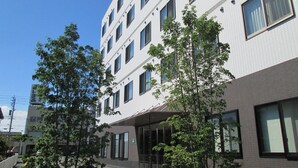 A multi-story building with a modern architectural design, featuring a mix of brick and white exterior walls, large windows, and a covered entrance area. - Okawa Riverside Hotel (Okawa)
