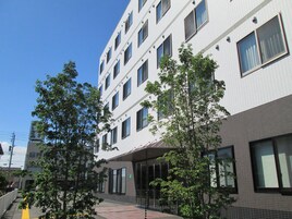 Un edificio de varios pisos con un diseño arquitectónico moderno, que presenta una combinación de paredes exteriores de ladrillo y blancas, ventanas amplias y una zona de entrada cubierta.